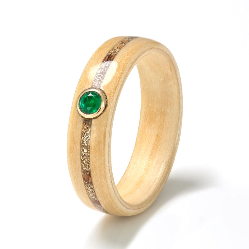 Apple wood ring with a centred inlay of vine wood and gold shavings, meeting at a round emerald in a gold bezel setting